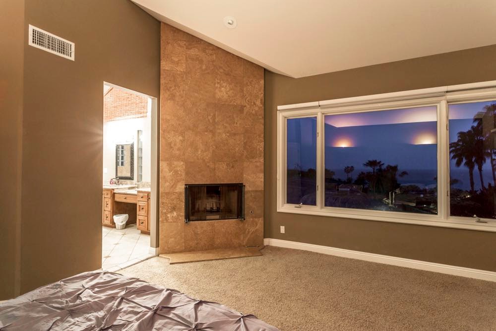 Interior bedroom with fireplace, panoramic ocean view windows, beige carpet, and coastal furnishings