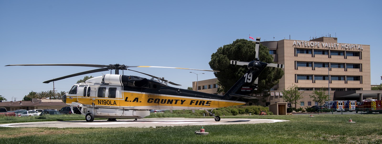 Exterior view of medical center with LA County Fire helicopter on landing pad, building facade, and landscaping visible