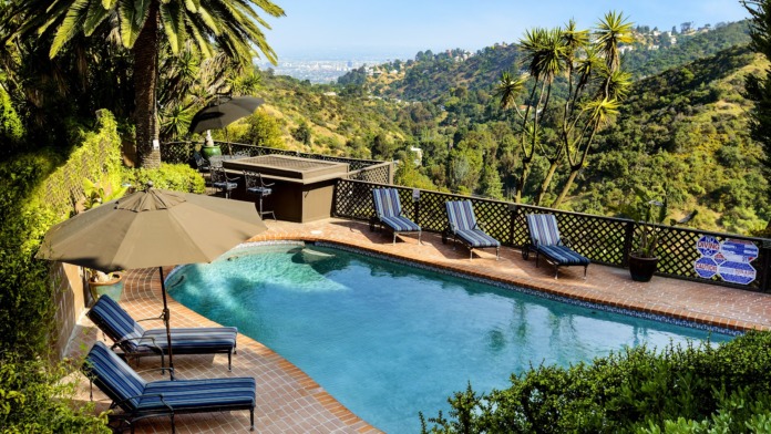 Outdoor pool area with lounge chairs, umbrellas, and panoramic hillside views of Los Angeles landscape