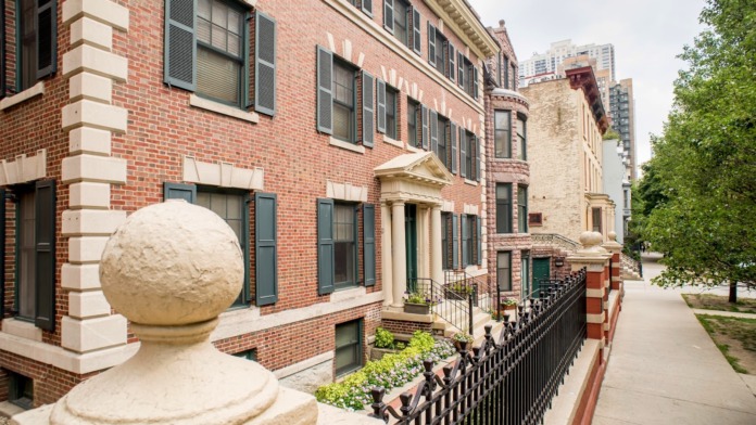 Exterior view of historic red brick building with white stone trim, arched entrance, black shutters, and manicured landscaping