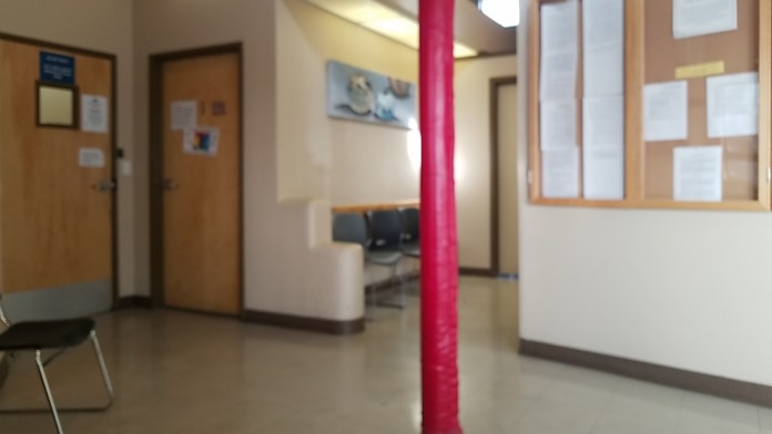 Interior hallway showing wooden doors, red support column, reception area with bulletin boards and signage
