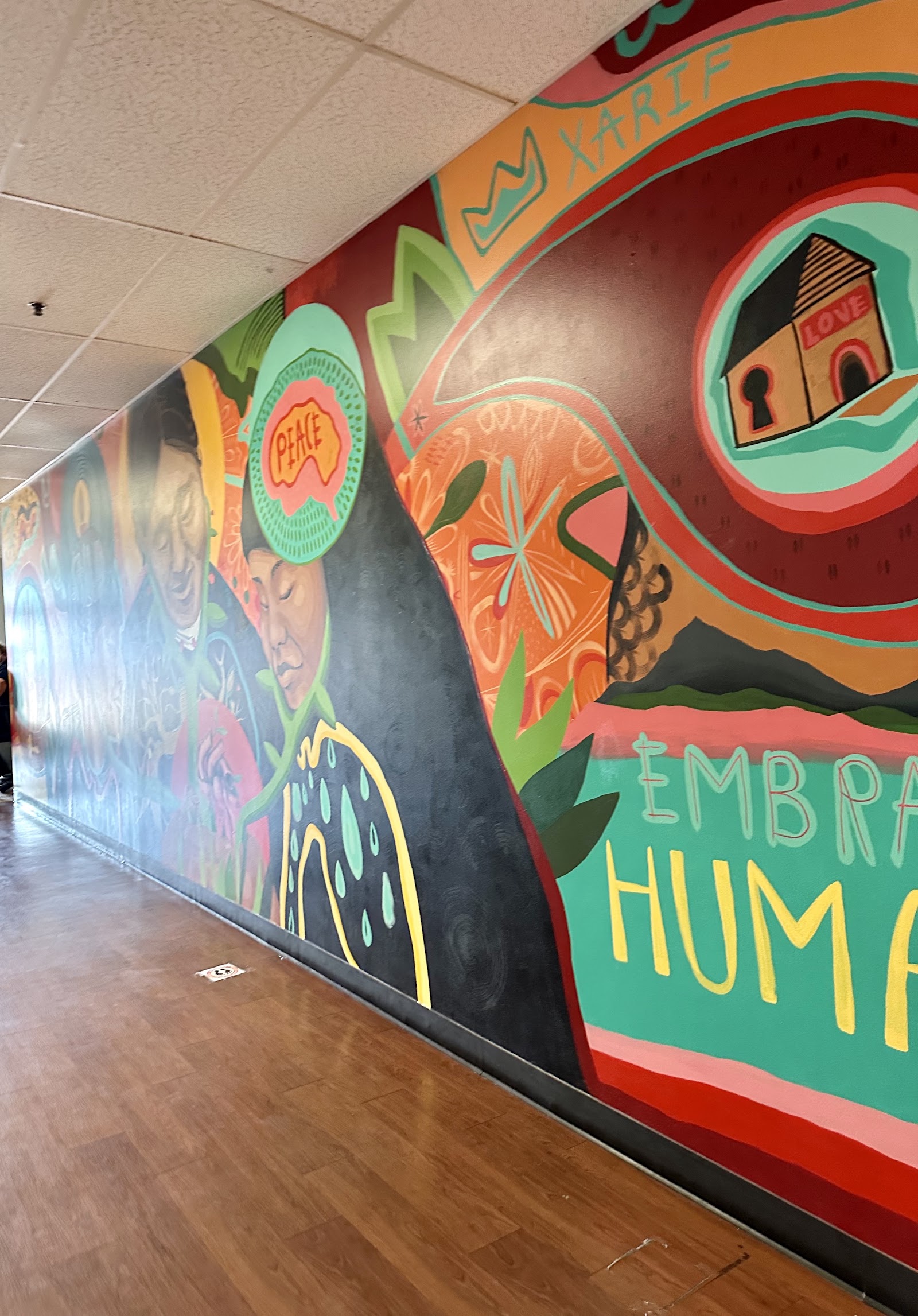 Interior hallway corridor featuring large colorful mural with abstract peace and embrace-themed artwork on wooden floor