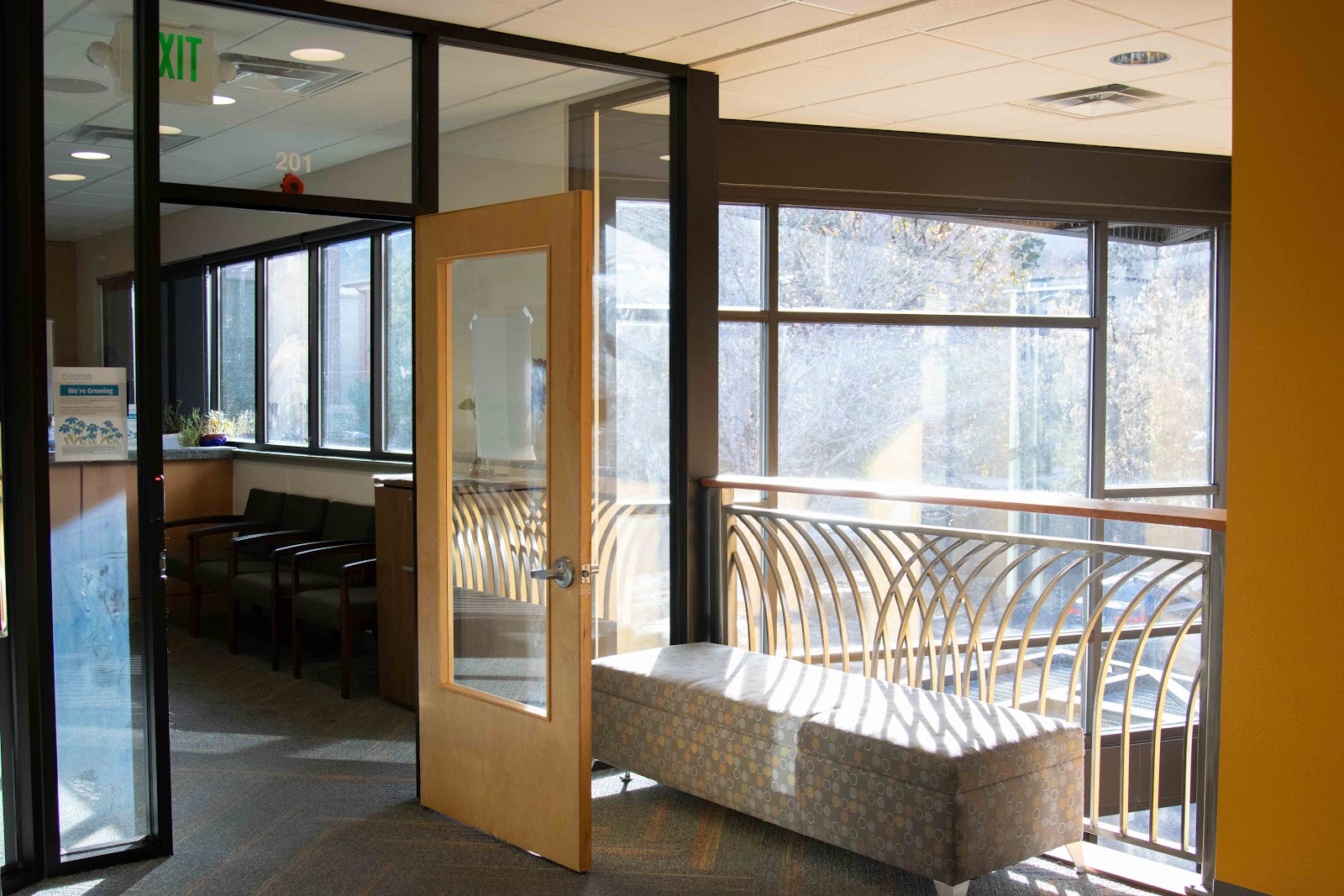 Interior hallway with glass doors, bench seating, yellow accent wall, and natural lighting from windows