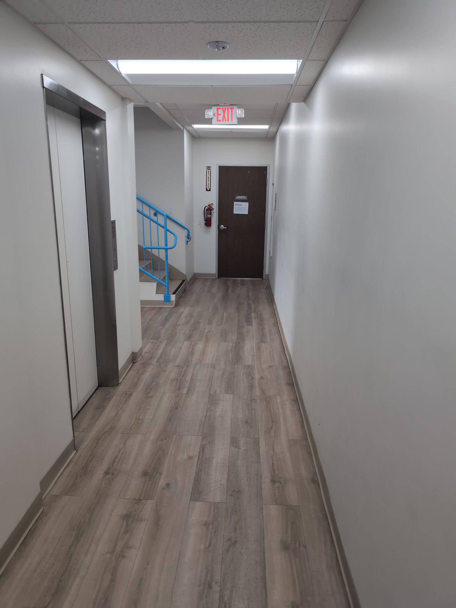 Interior hallway with wood flooring, blue spiral staircase, white walls, exit sign, and treatment facility doors