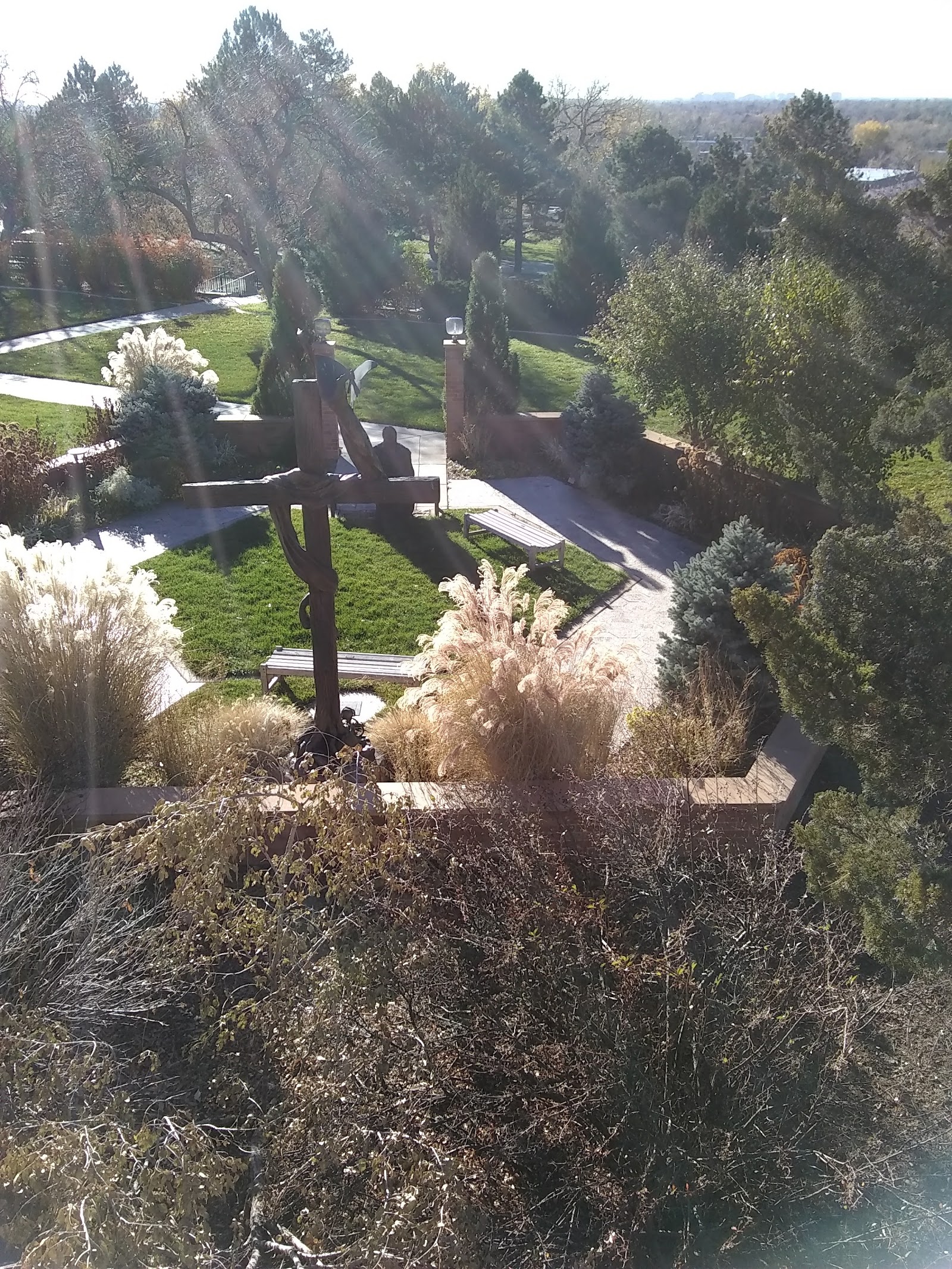 Outdoor grounds featuring large cross monument, pathways, manicured lawn, and surrounding mature trees.