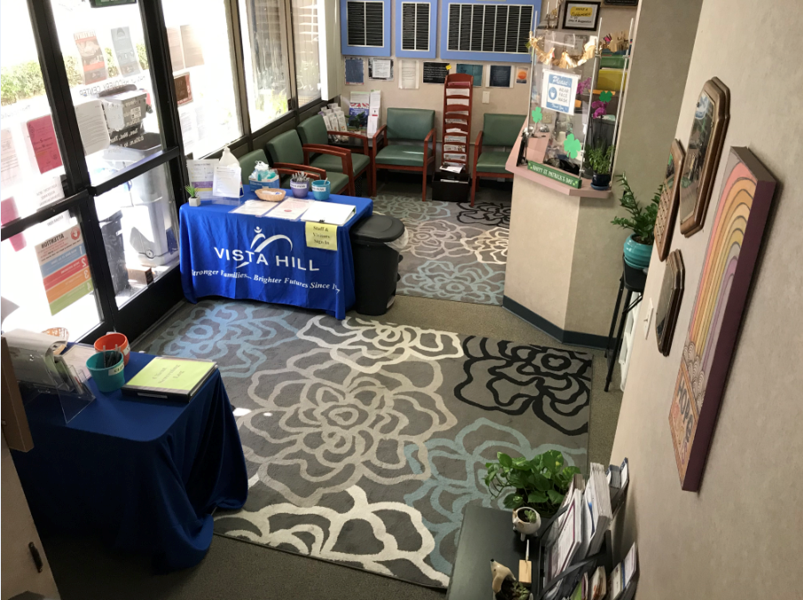 Interior entryway and lobby area with blue table displays, green seating chairs, blue signage, and window entrance to facility