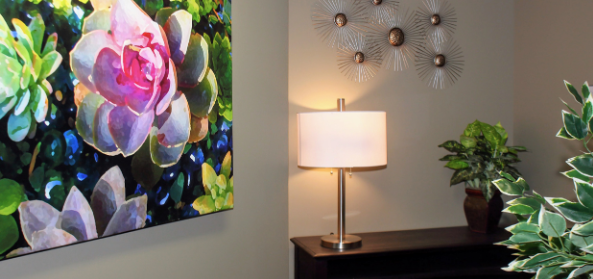 Interior lounge space with framed botanical artwork, table lamp, decorative wall sculpture, and potted plant