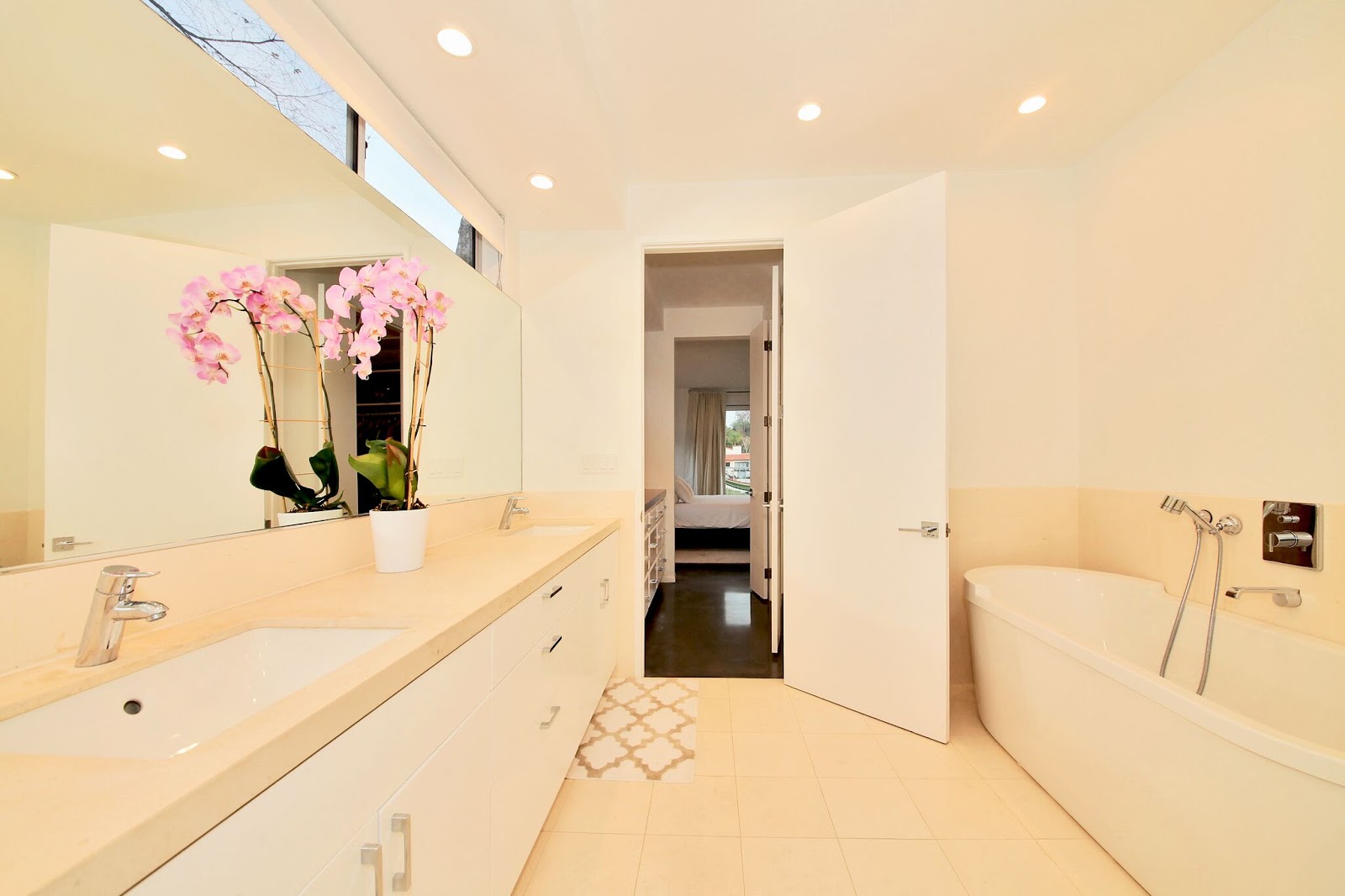 Interior spa bathroom with dual vanities, soaking tub, large mirror, orchid arrangement, and natural window lighting