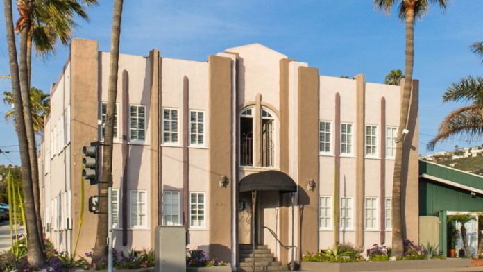 Exterior of Art Deco-style treatment center building with cream and tan facade, palm trees, and main entrance with dark awning