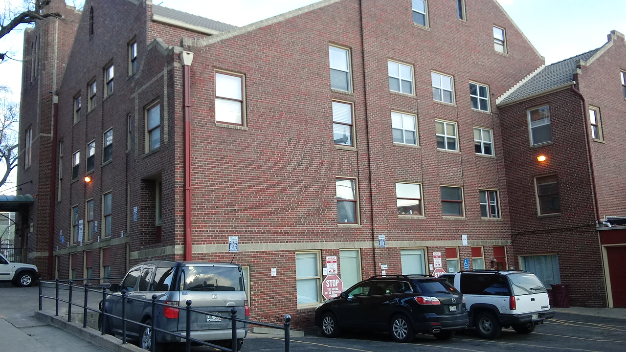 Exterior of multi-story brick building showing entrance doors, windows, handicap accessible parking, and street view