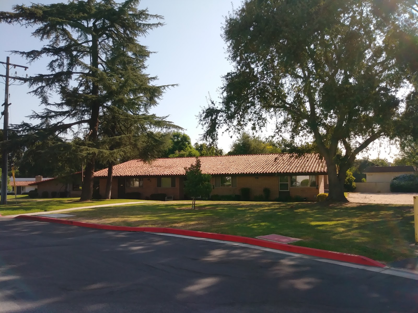 Single-story building with terra-cotta roof surrounded by mature trees on lawn