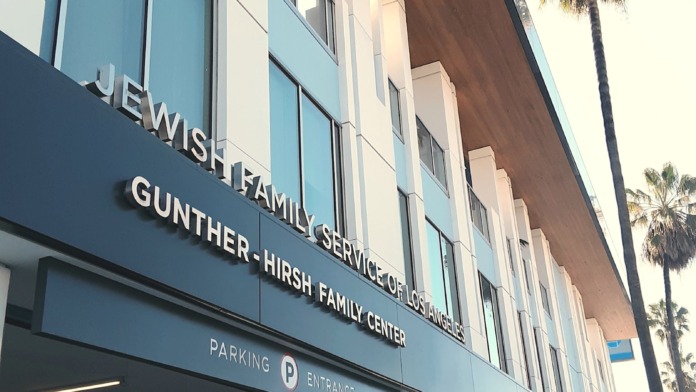 Exterior view of treatment facility entrance with blue and white facade, signage, and parking entrance visible, palm trees in background.