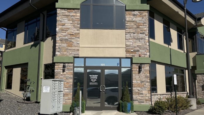 Exterior of New Paradigm Counseling facility showing main entrance with stone and green stucco facade, Suite 101 signage, and landscaping