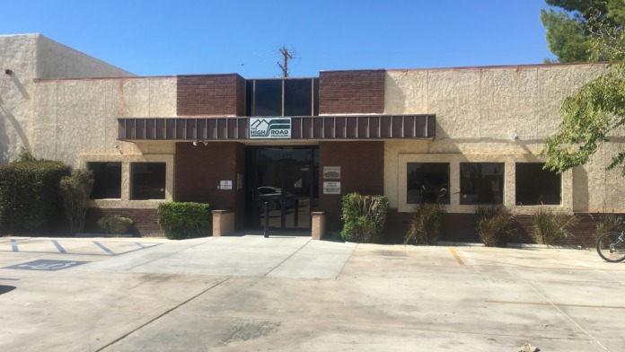 Exterior view of treatment facility showing main entrance with signage, brick and concrete facade, parking area, and landscaping
