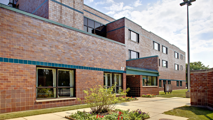 Exterior view of brick treatment facility with main entrance, landscaped courtyard with flowering plants, and paved walkway