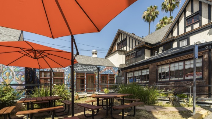 Exterior courtyard featuring covered brick patio entrance with red umbrellas, picnic seating, and Tudor-style building facade