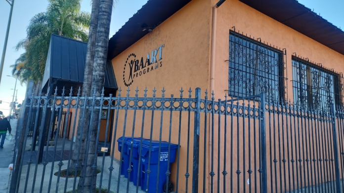 Exterior of BAART Programs Beverly facility showing orange stucco building with blue metal fence, decorative spikes, and palm trees