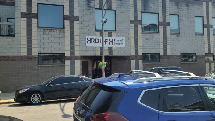 Exterior of HRDI medication assisted treatment facility showing brick and stone facade, signage, windows, and front parking area