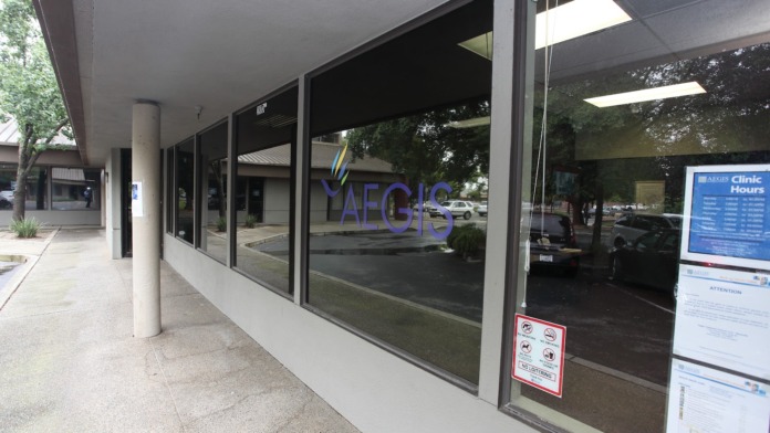 Exterior front entrance showing Aegis Treatment Centers purple logo signage on glass storefront with covered walkway and parking area visible