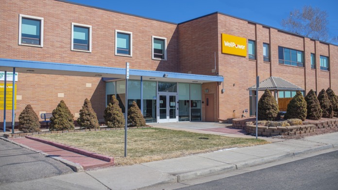 Exterior view of brick building with main entrance, blue awning, landscaping, and WellPower signage