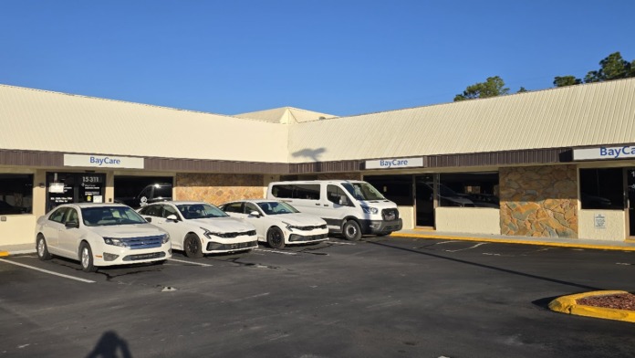 Exterior view of BayCare Behavioral Health facility showing main entrance, parking lot with vehicles, and building facade with stone accents