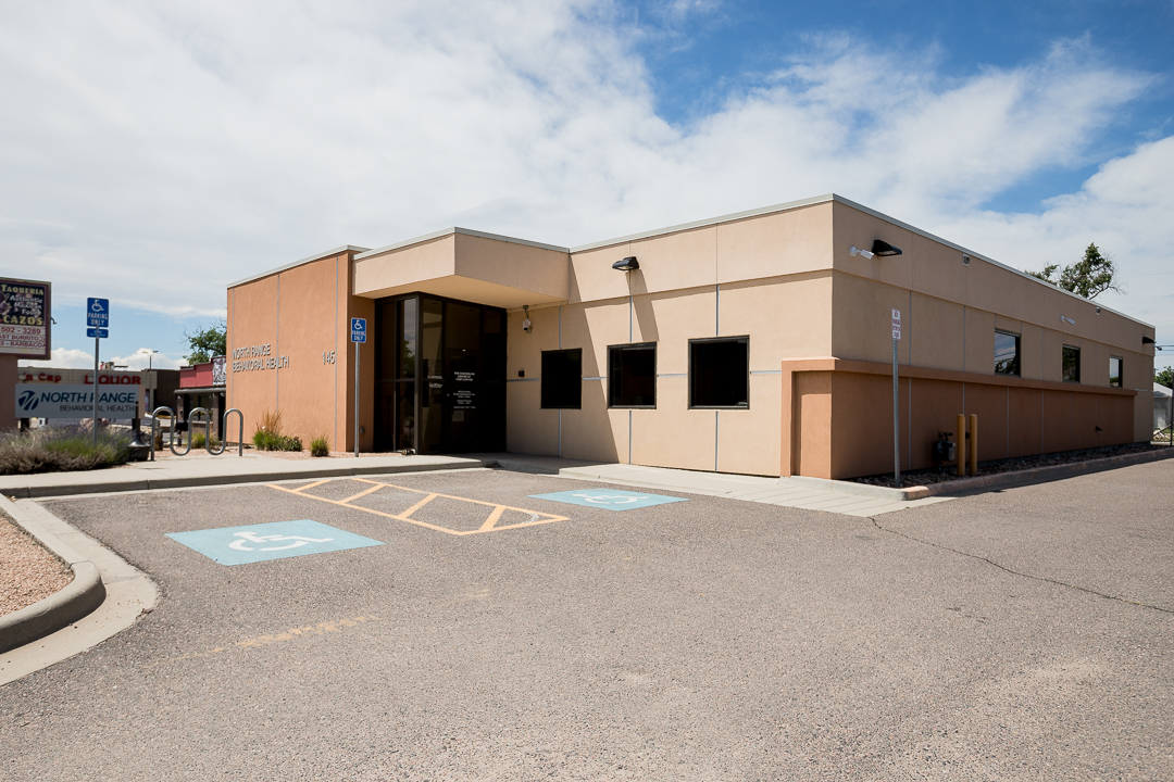 Front corner entrance of treatment facility with accessible parking spaces, main entry door, and neighboring commercial buildings