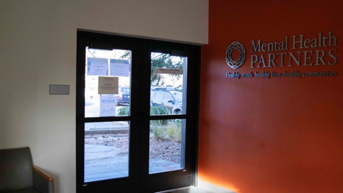 Interior main entrance with Mental Health Partners branding, glass doors, reception area, and parking view