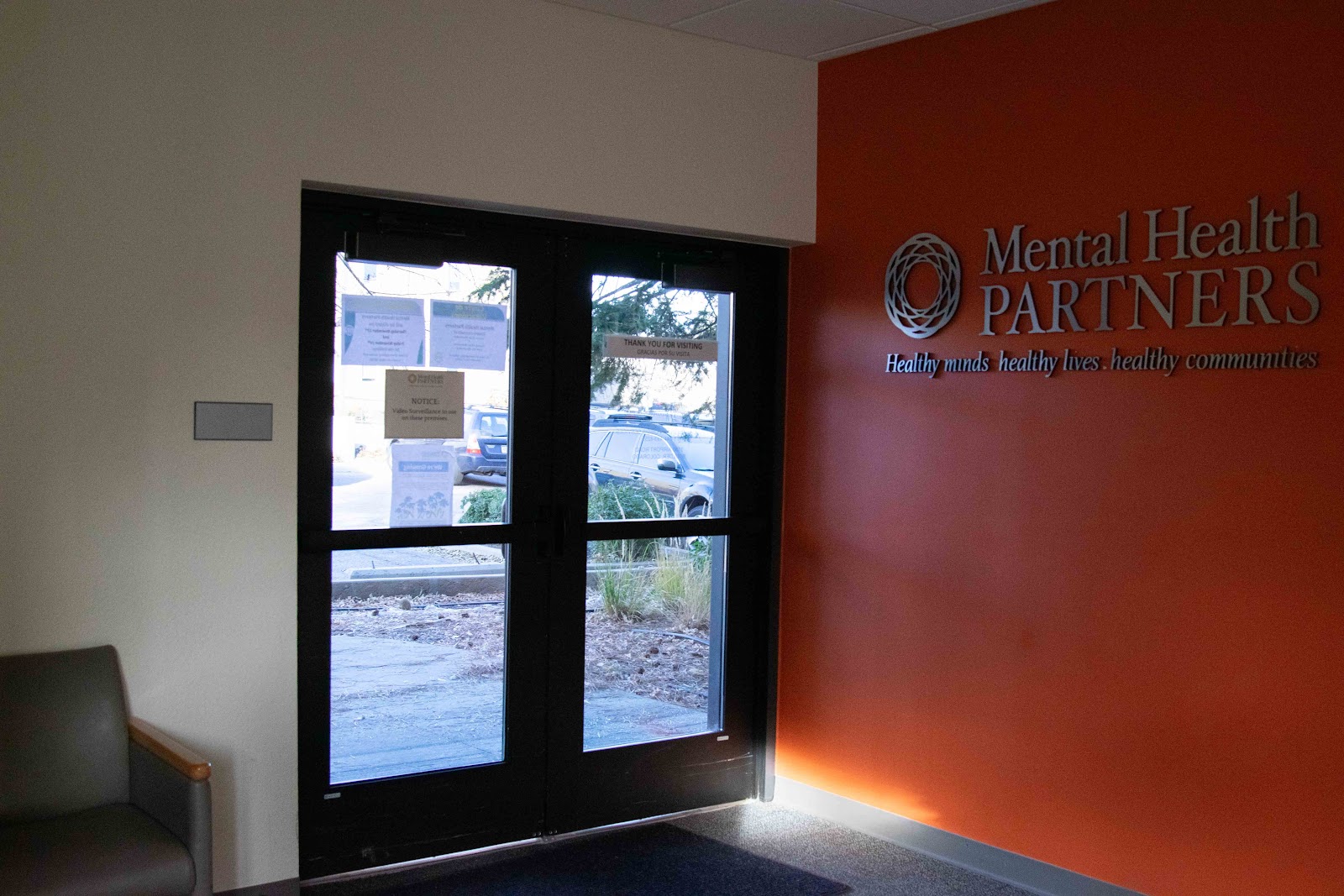 Interior main entrance with Mental Health Partners branding, glass doors, reception area, and parking view