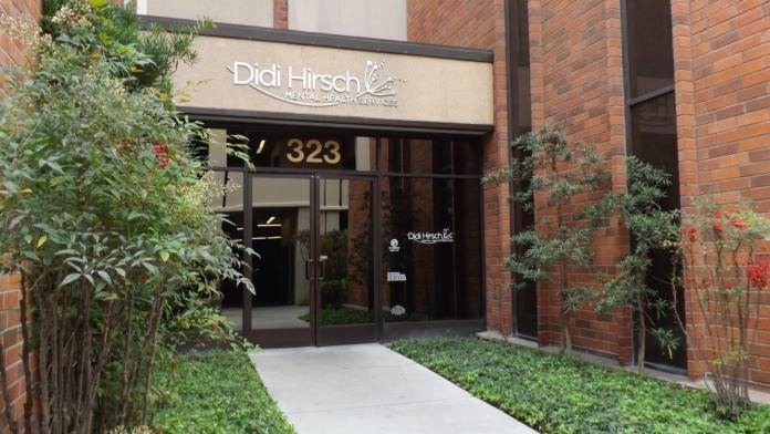 Exterior entrance of Didi Hirsch Mental Health Services showing main doors, address number 323, landscaped planters, and facility branding on brick building