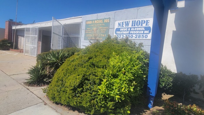 Exterior view of New Hope Drug & Alcohol Treatment Program building with blue signage, white metal gates, and landscaped shrubs along the sidewalk