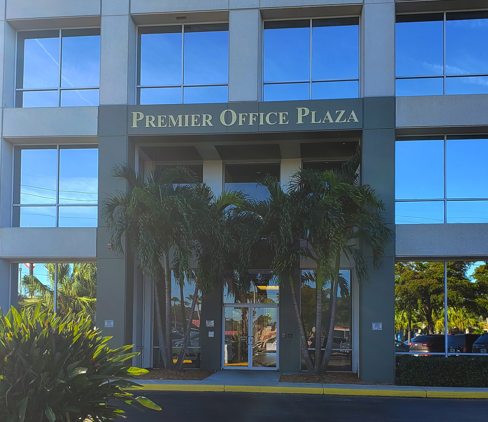 Exterior main entrance featuring Premier Office Plaza signage, glass doors, and tropical plantings