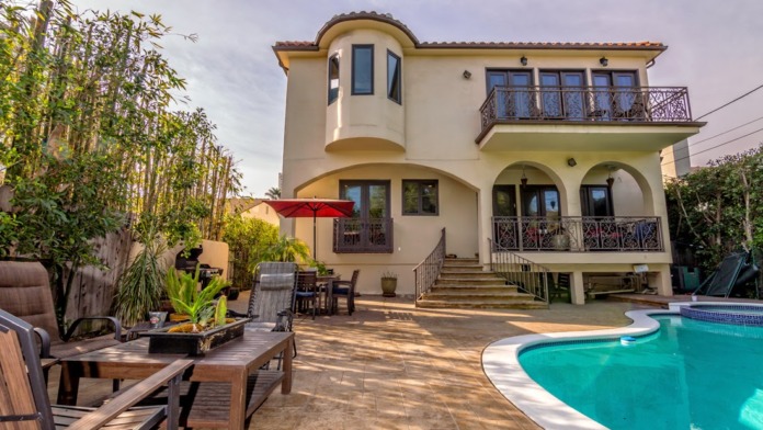 Exterior view of Mediterranean-style facility with main entrance, swimming pool, lounge seating, and manicured grounds