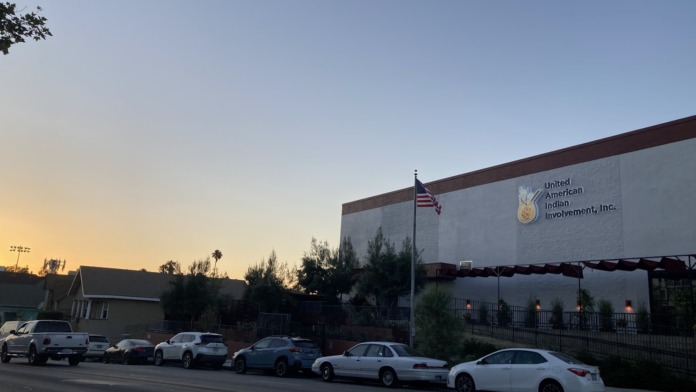 Exterior view of United American Indian Involvement facility showing white brick building with maroon stripe, signage, American flag, and street parking