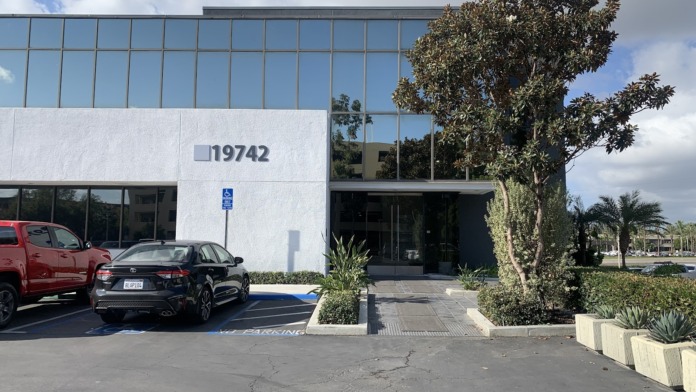 Exterior of modern treatment center showing white facade with address 19742, glass windows, front entrance, and parking area with vehicles