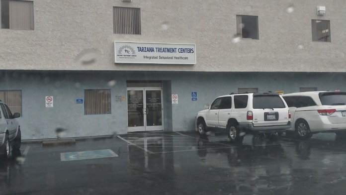 Exterior two-story treatment center building with signage, windows, parked vehicles, and wet ground from rain