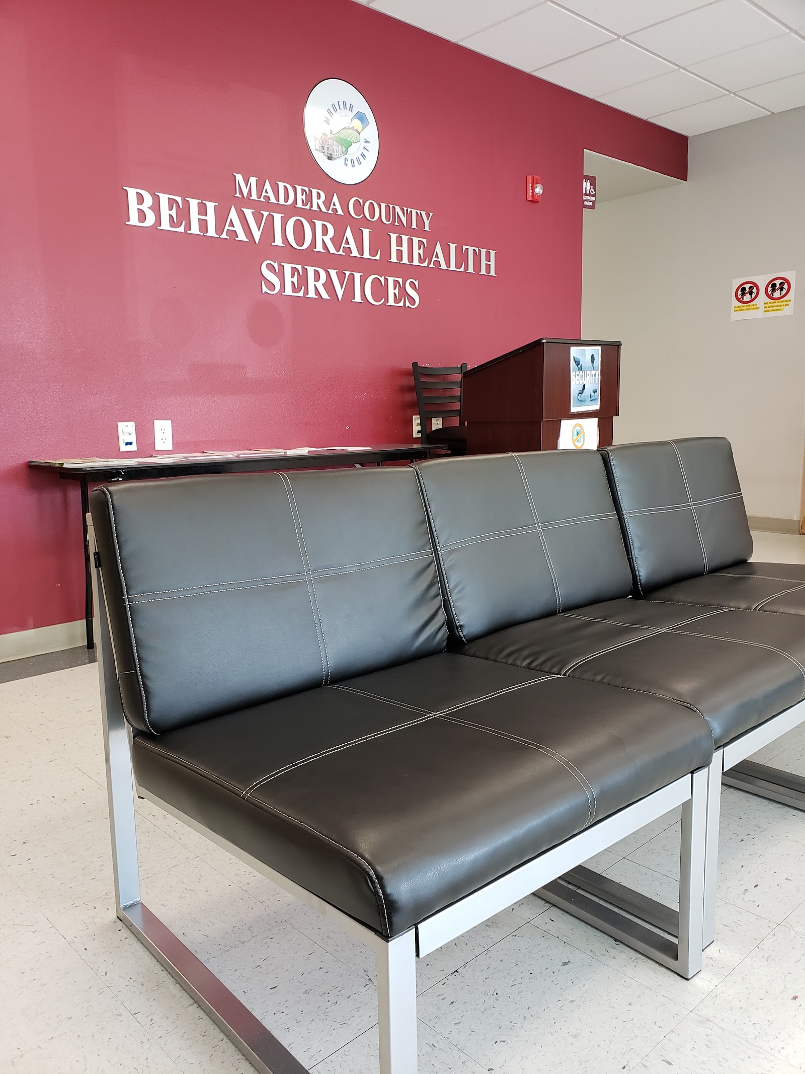 Interior reception area with beige curved desk, black seating, and signage for Madera County Behavioral Health Services