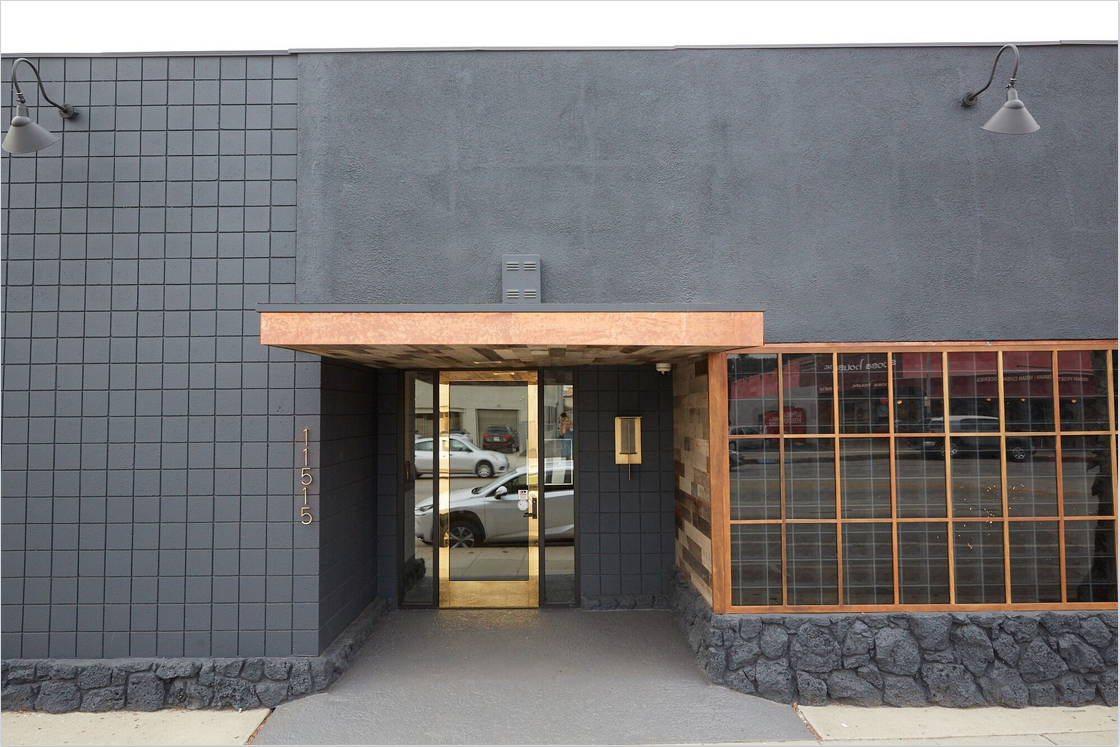 Exterior front facade with dark charred wood cladding, glass entry doors, metal accents, and stone base