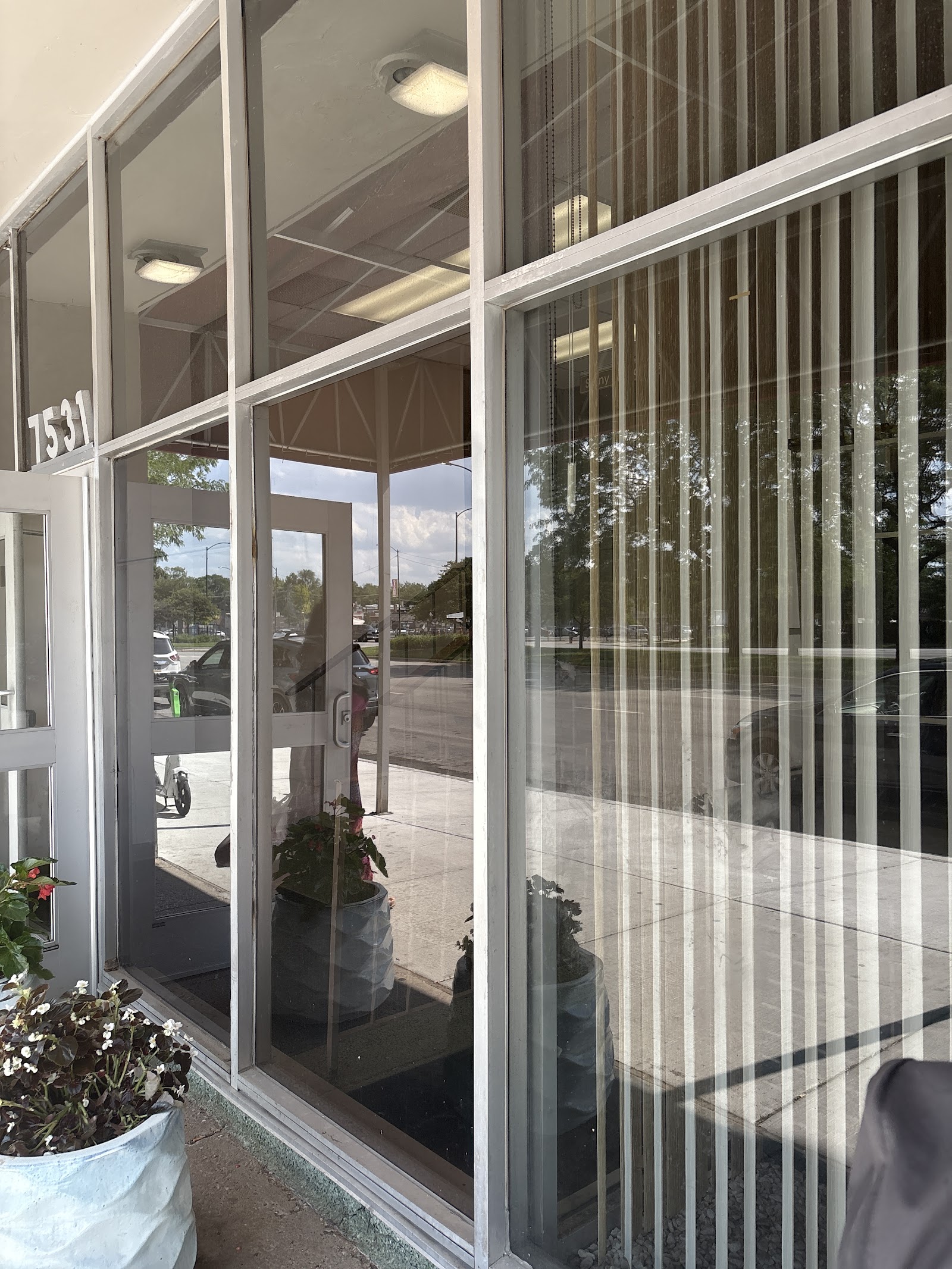 Exterior glass and metal framed entrance with large windows, address 7531 displayed on storefront, parking lot visible through windows