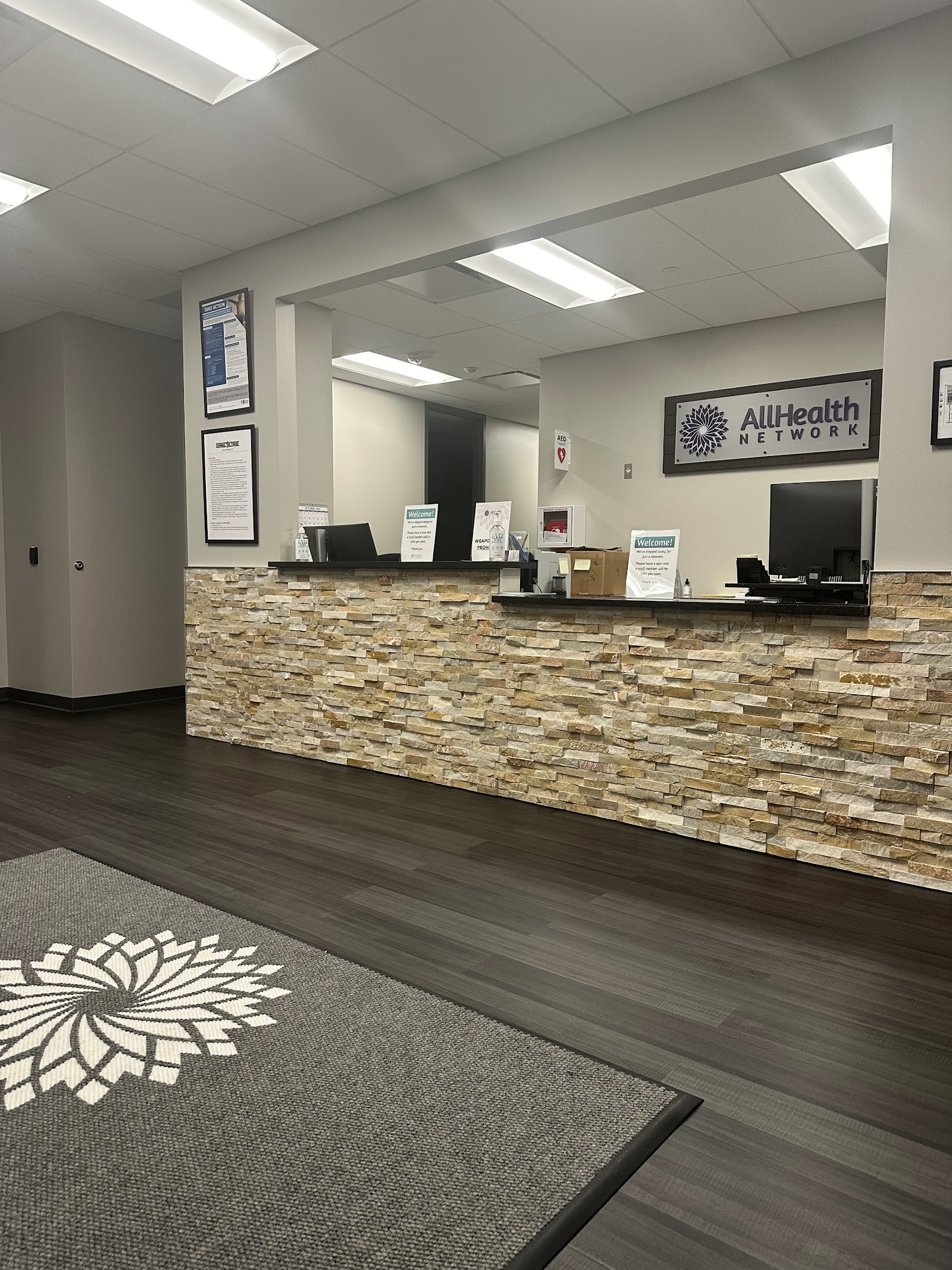 Interior lobby featuring stone accent wall, AllHealth Network branding, and contemporary reception counter with plants