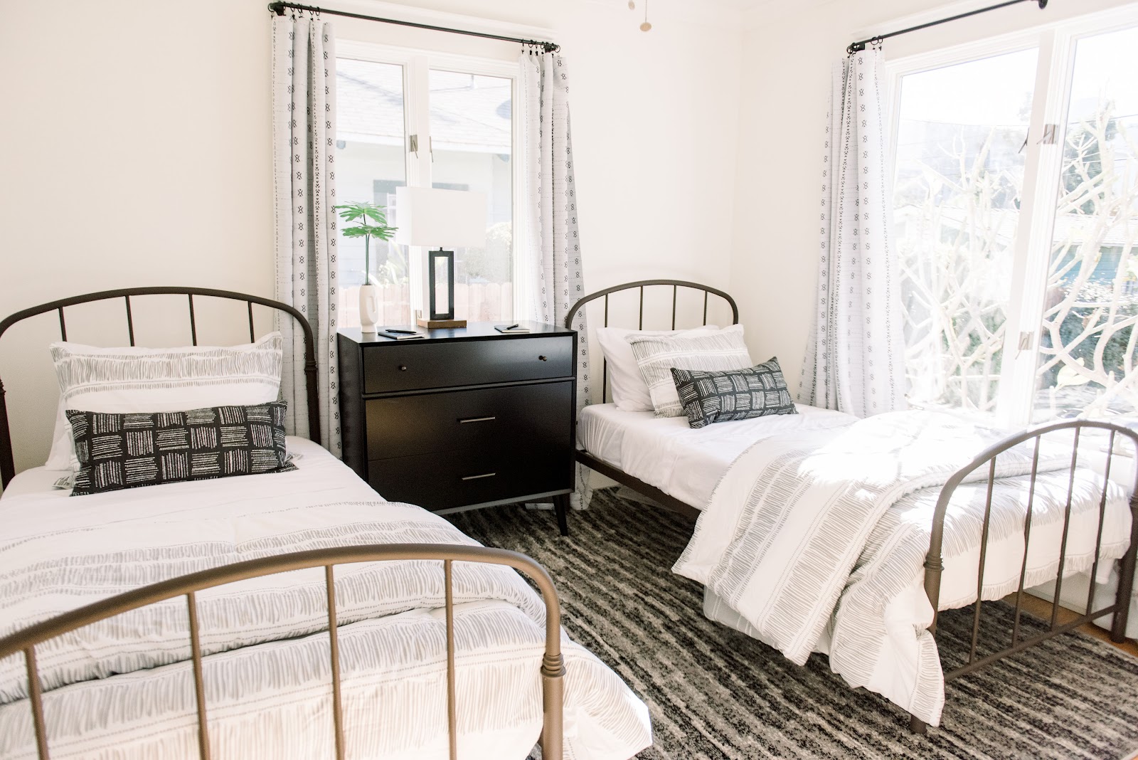 Interior patient bedroom with three beds with metal frames, shared dresser, and windows with sheer curtains providing natural light