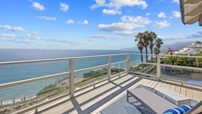 Exterior oceanfront deck with comfortable lounge chairs, ocean views, and glass railing overlooking Pacific Coast