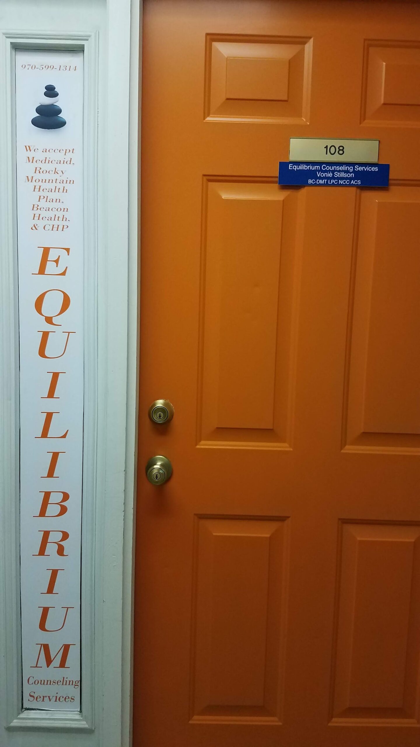 Exterior office door with orange finish showing room number 108 and facility signage with business credentials and phone number
