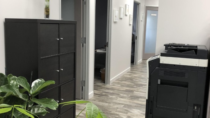 Interior hallway showing multiple treatment room doors, black cabinetry, potted plants, and water cooler along wood-look flooring