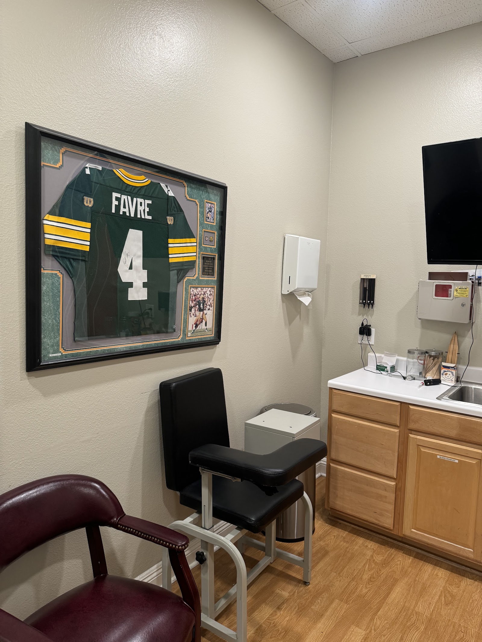Interior office with wooden desk, white sink, wall-mounted television, and shelving with supplies and decorative items