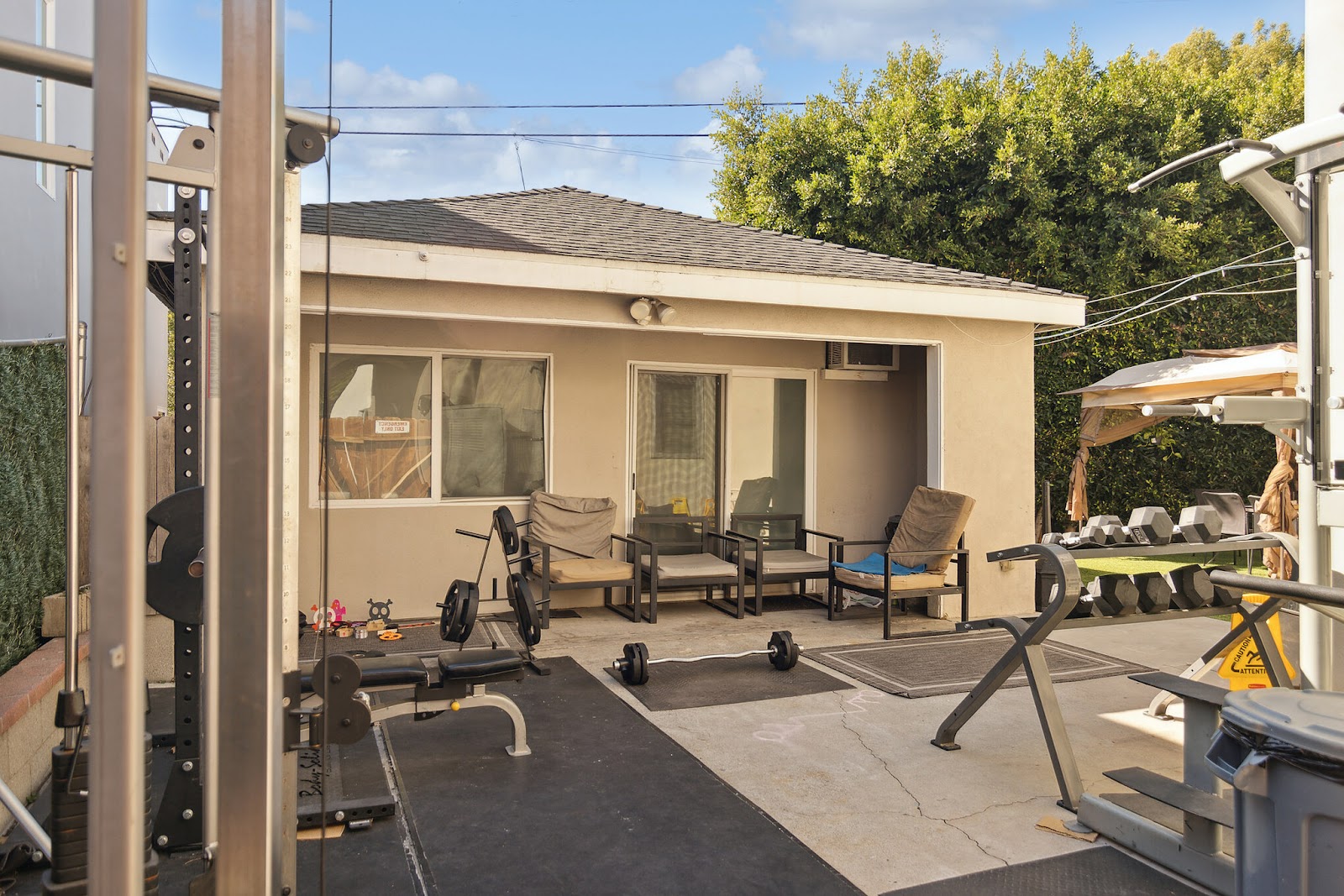 Outdoor fitness patio with exercise equipment, lounge seating, concrete flooring, pergola structure, and landscaped grounds