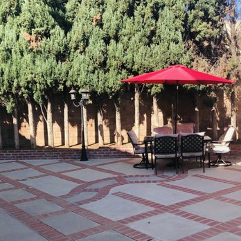 Exterior patio area with red umbrella, seating furniture, tall trees, and decorative brick pavers