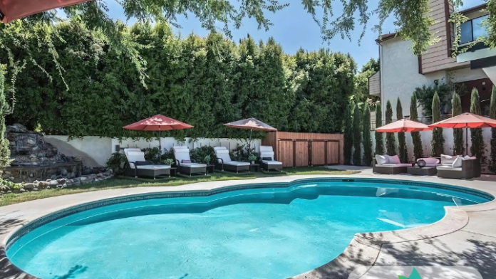 Exterior showing curved swimming pool with turquoise water, red umbrellas, white lounge chairs, and manicured landscaping.