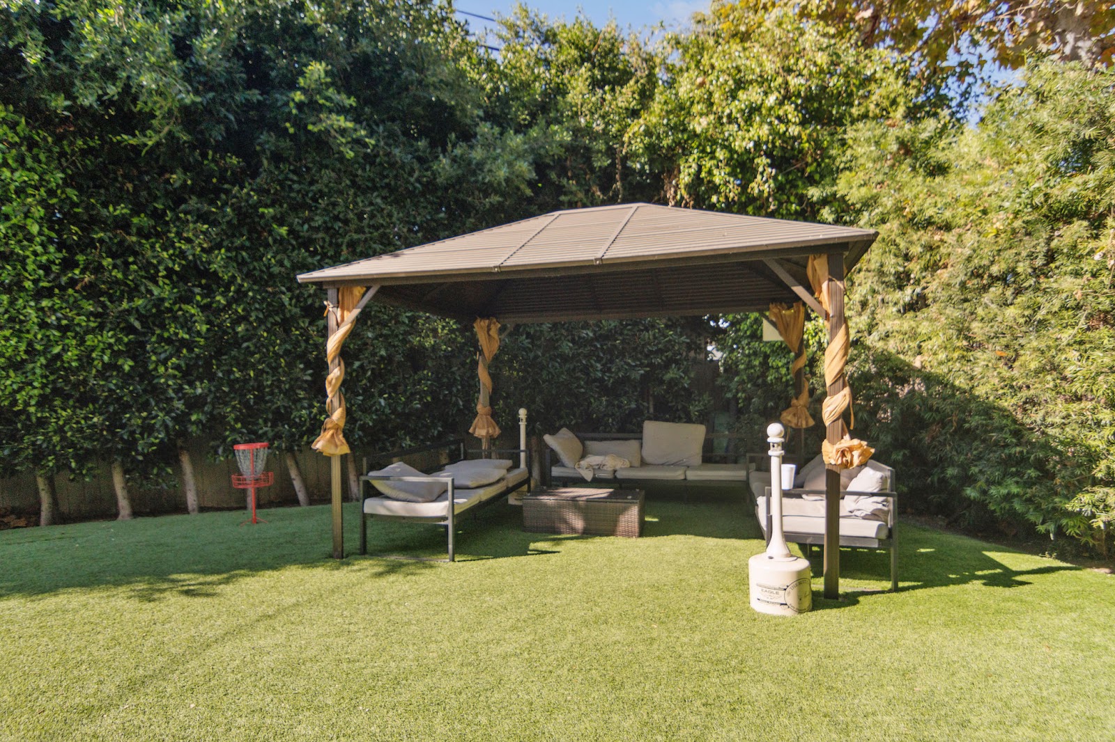 Outdoor courtyard with wooden pergola structure, comfortable seating, manicured lawn, and mature trees surrounding patio space