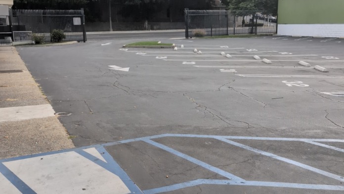 Exterior parking lot with painted spaces, green facility building facade, metal fence, and surrounding trees