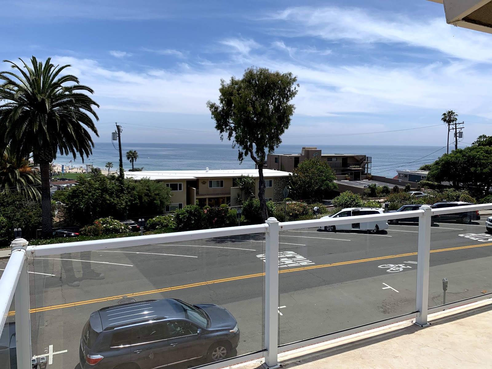 Exterior parking area with vehicles, palm trees, coastal landscape, and ocean visible in distance
